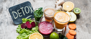 Eine Auswahl an Detox-Getränken, einschließlich Säfte und Smoothies, angeordnet mit Gemüse, Obst und Kräutern.