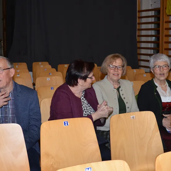 Vier Erwachsene, drei Frauen und ein Mann, sitzen in einem Auditorium, wobei eine Frau applaudiert.