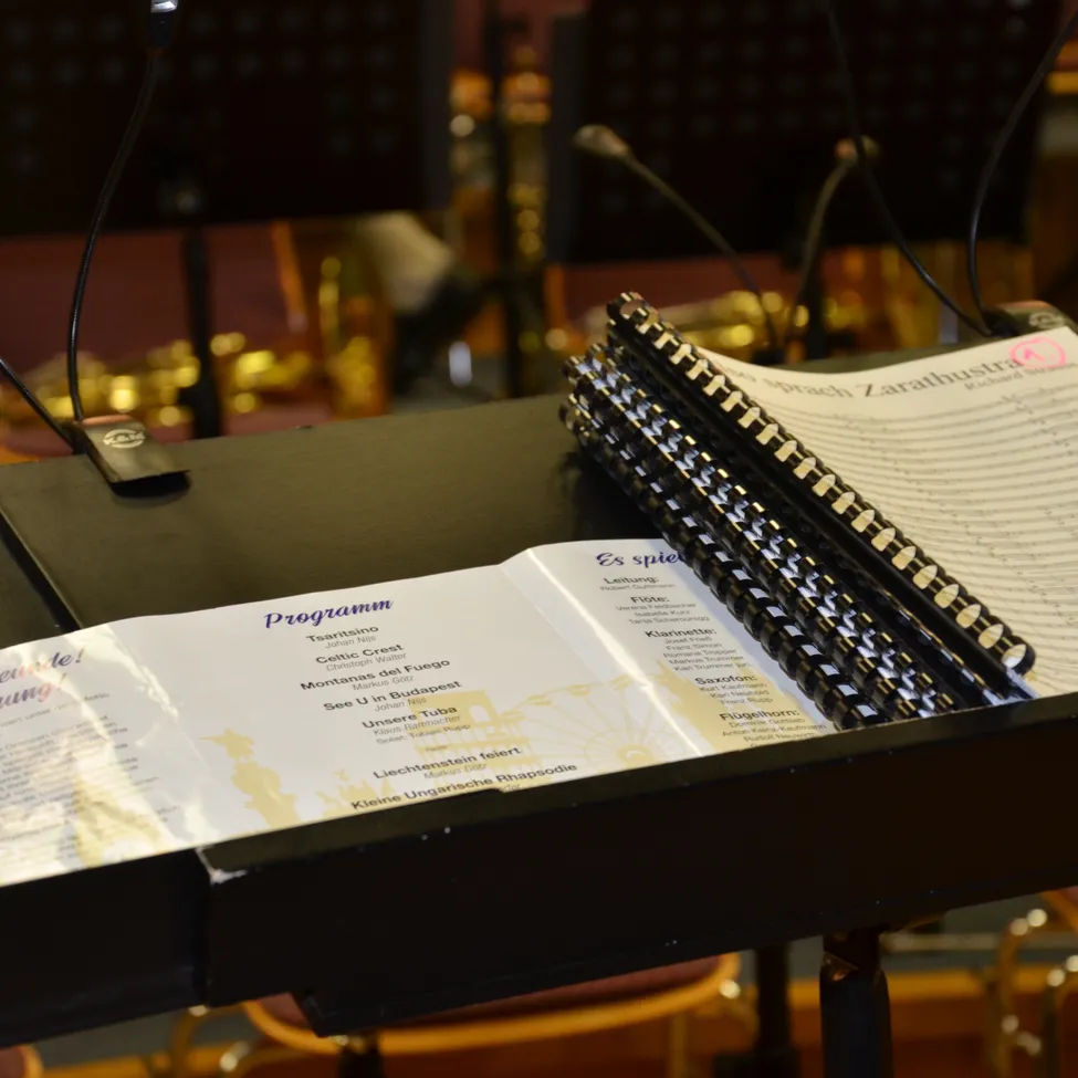 Ein Musikpult mit offenem Programmheft und Mikrofonen in einem Konzertsaal. Das Heft hat ein Programm mit dem Titel 'Brach Zarathustra'.