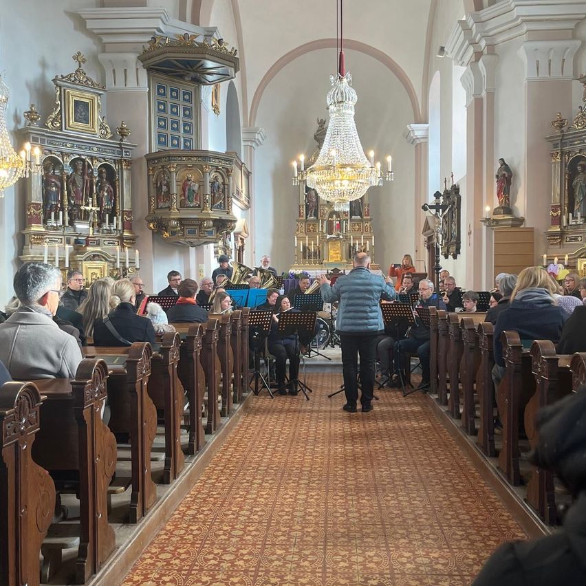Eine Band tritt in einer Kirche auf. Die Band steht in der Mitte der Kirche, während das Publikum auf den Bänken auf beiden Seiten sitzt.