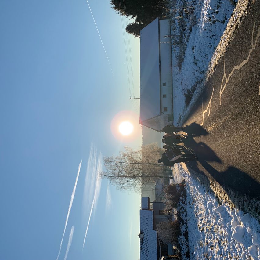 Luftaufnahme einer Straße mit einem hellen Sonnenschein, Schnee an der Seite und mehreren Menschen, die darauf laufen.
