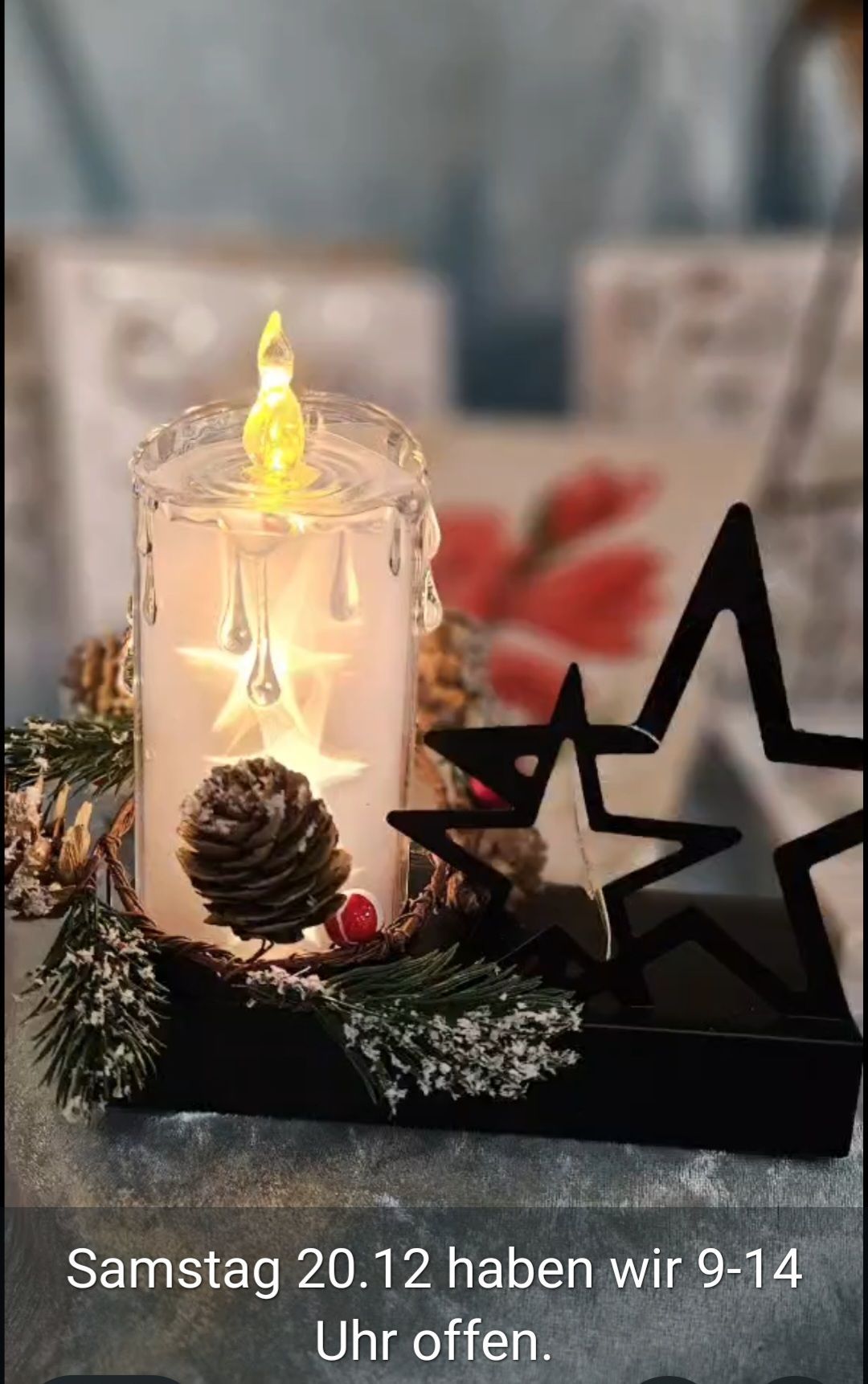 Eine brennende Kerze mit einer gelben Flamme in einem klaren Glasbehälter. Die Kerze hat ein sternförmiges Design und einen Tannenzapfen oben. Es gibt zwei sternförmige Dekorationen an der Seite.