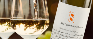 Eine Weinflasche mit dem Etikett 'Seltenhammer' wird in ein Weinglas gegossen. Das Glas ist mit Wein gefüllt, und die Flasche steht auf einem Tisch.