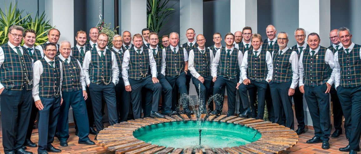 Eine Gruppe von Männern in karierten Westen und Krawatten posiert für ein Foto neben einem Brunnen.