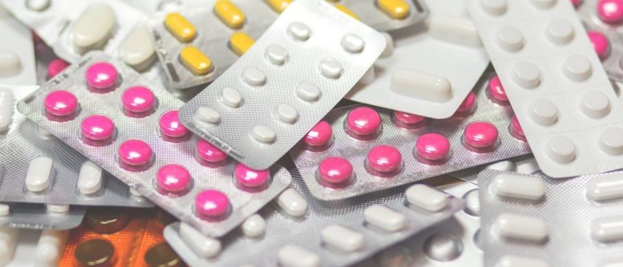 Ein Stapel verschiedener Medikamente, einschließlich weißer, gelber und rosa Pillen, einige in Blisterpackungen und andere in Kapseln, ordentlich gestapelt.