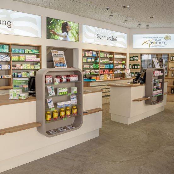 Eine Apotheke mit einem schmerzfreien Schild darüber. Regale mit verschiedenen Produkten und ein Computer auf der Theke. Die Apotheke hat ein modernes und sauberes Design.