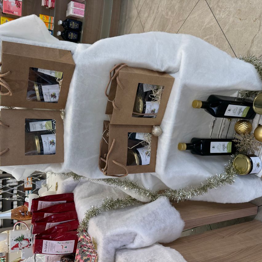 Eine Präsentation mit mehreren Geschenkboxen, die in weißem Stoff eingewickelt und mit Weihnachtsdekorationen geschmückt sind. Die Schachteln enthalten verschiedene Flaschen und Gläser mit Produkten.