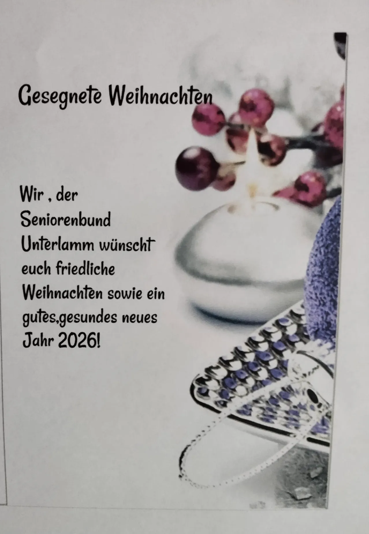 Eine Karte mit einem festlichen Weihnachtsdesign zeigt eine lila Blume und einen dekorativen Anhänger. Es steht 'Gesegnete Weihnachten' und wünscht friedliche Weihnachten und ein gesundes neues Jahr 2026.
