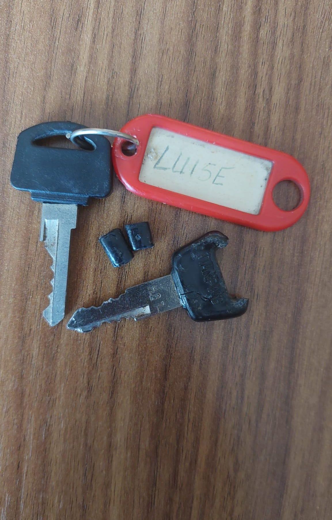 Ein schwarzer Schlüssel, ein zerbrochener Schlüssel, ein zerbrochener Schlüsselkopf und ein roter Schlüsselanhänger mit dem Namen Lu15E sind auf einer Holzoberfläche.