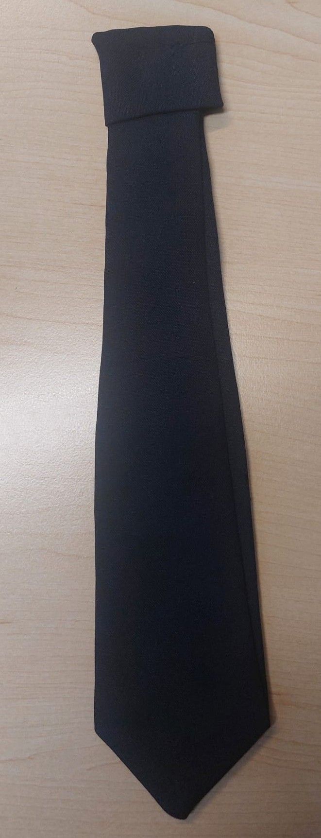 Eine Nahaufnahme eines schwarzen Stoffrandes, möglicherweise eines Rocks, mit einer sichtbaren hölzernen Oberfläche auf der Seite.