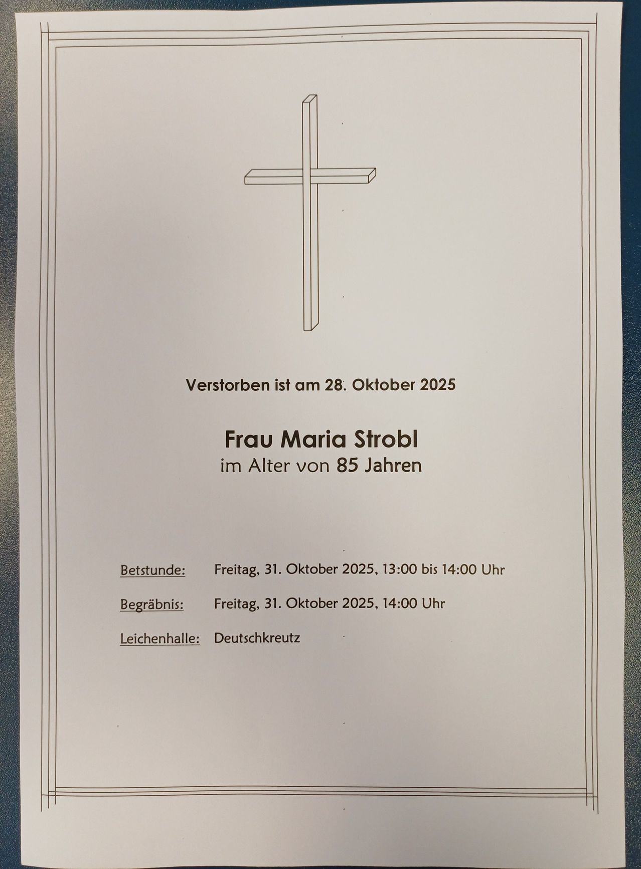 A memorial card with a cross symbol reads: 'Frau Maria Strobl died at age 85 on October 28, 2025. Burial: Friday, October 31, 2025, 13:00-14:00. Funeral: October 31, 2025, 14:00. Location: Deutschkreutz.'