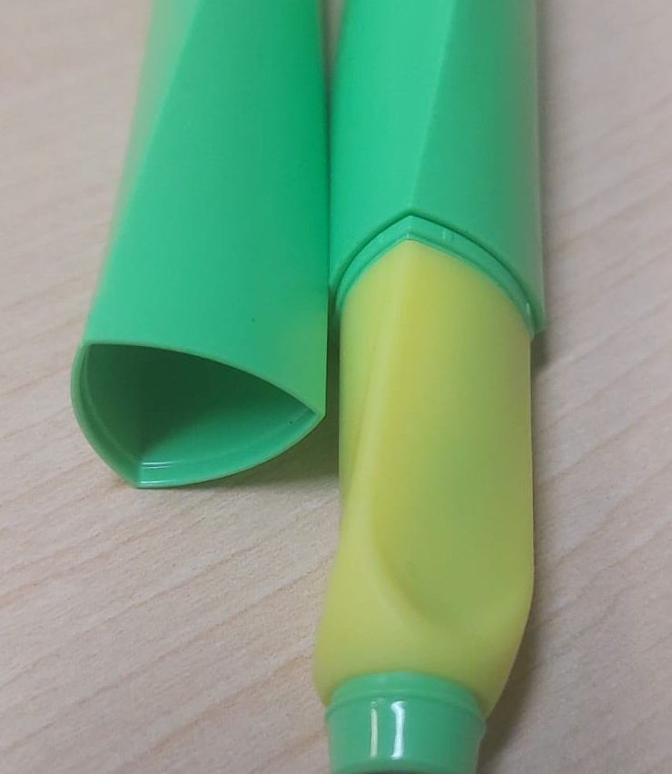 Two green cylindrical objects, possibly markers, are placed on a wooden surface. One is open, and the other has a yellow tip.