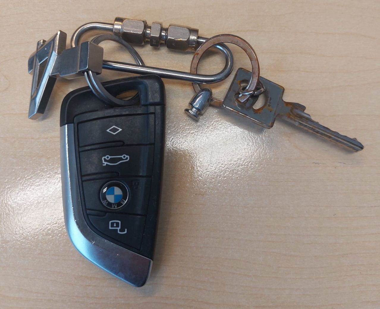 A BMW car key fob with two keys attached, one rusty and one with a metal clip, resting on a wooden surface.