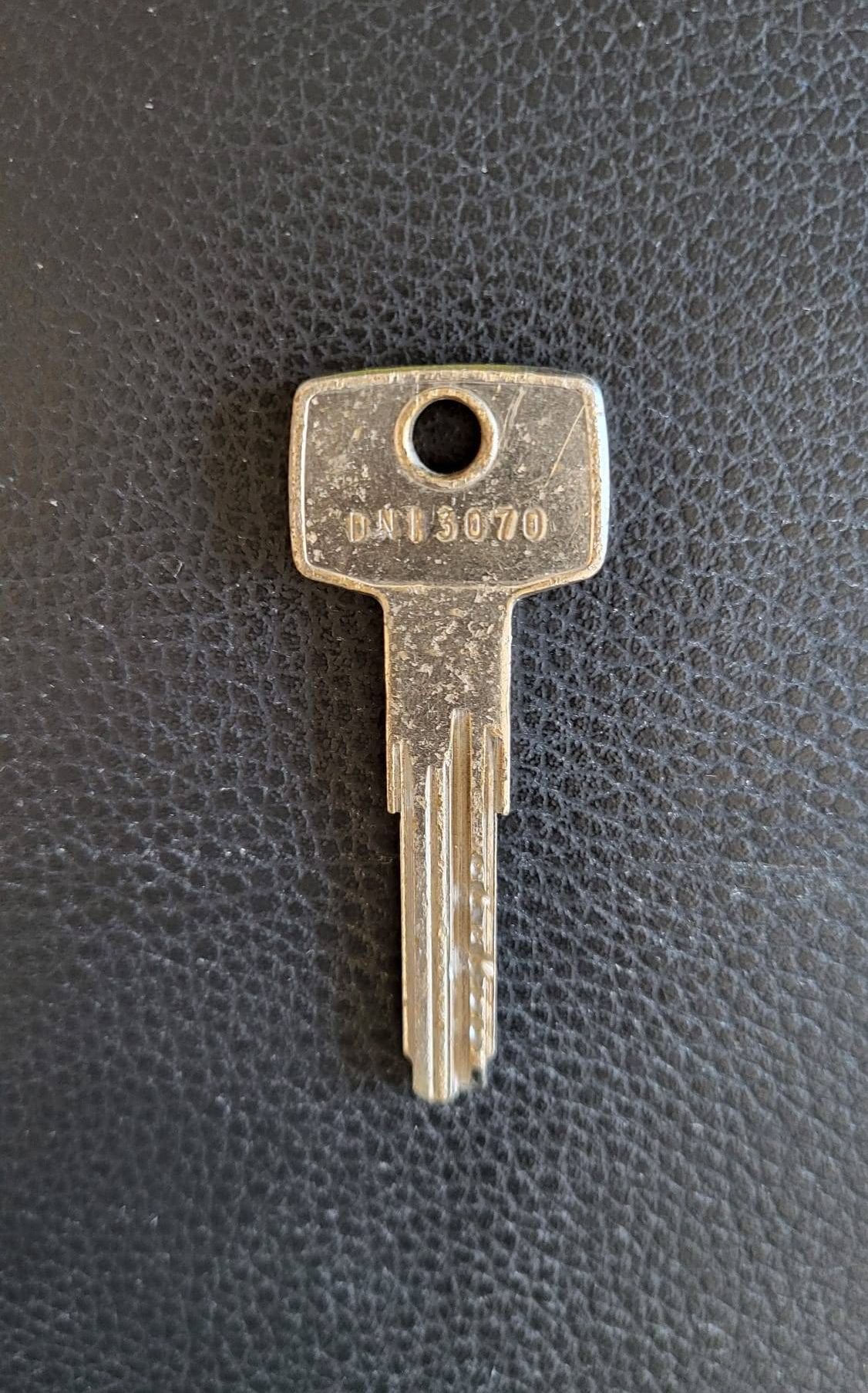 Ein metallischer Schlüssel mit der Bezeichnung DN15070 auf einer strukturierten schwarzen Lederoberfläche. Der Schlüssel hat ein Loch in der Mitte.