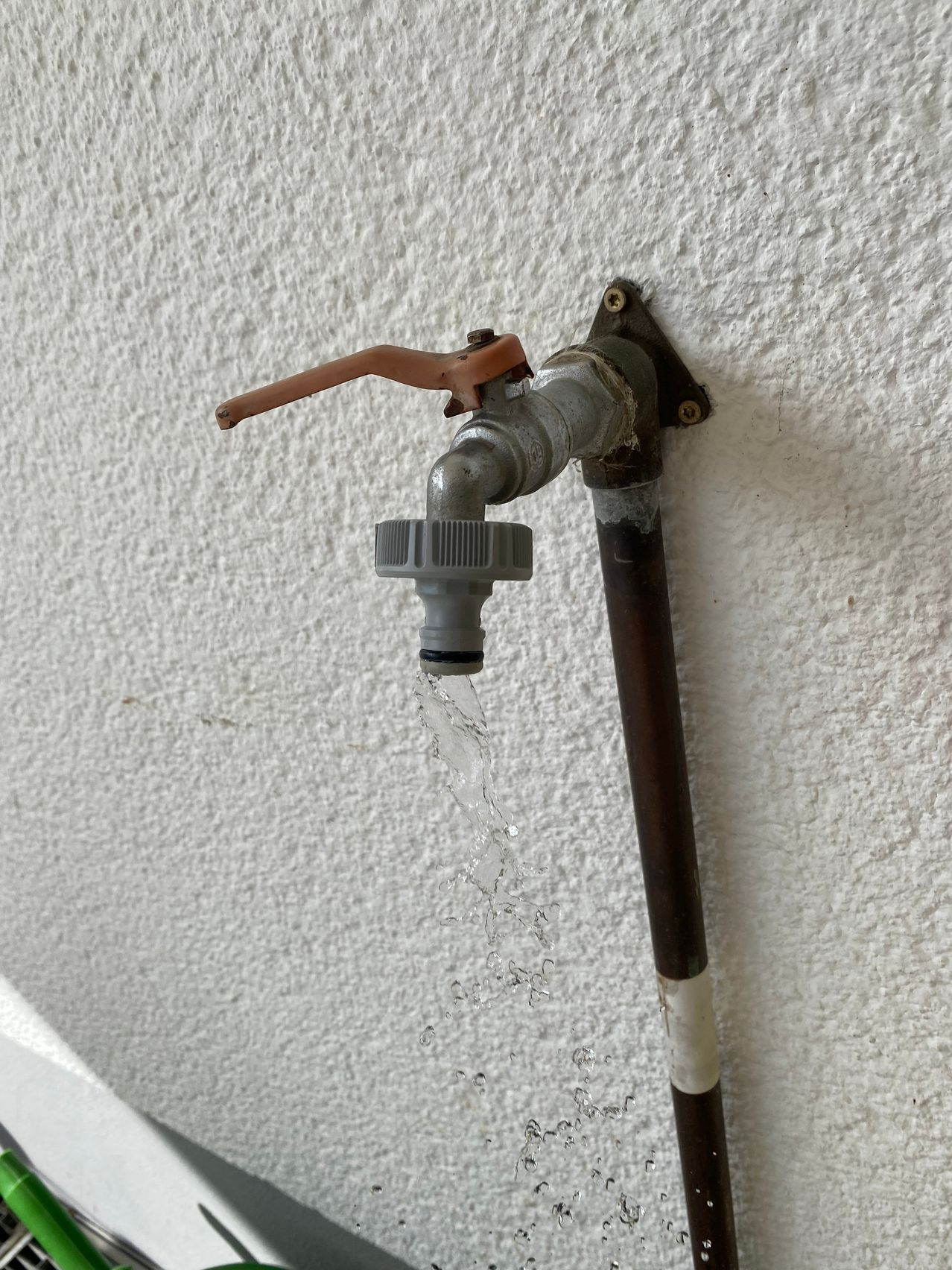 Ein Außenwasserhahn ist an einer weißen Wand montiert, aus dem offenen Hahn fließt Wasser.