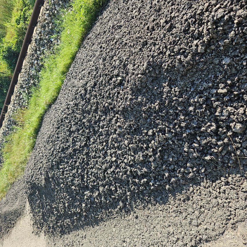 Eine Nahaufnahme eines grauen Schotterhaufens neben einer Eisenbahnlinie mit grünem Gras an der Seite.