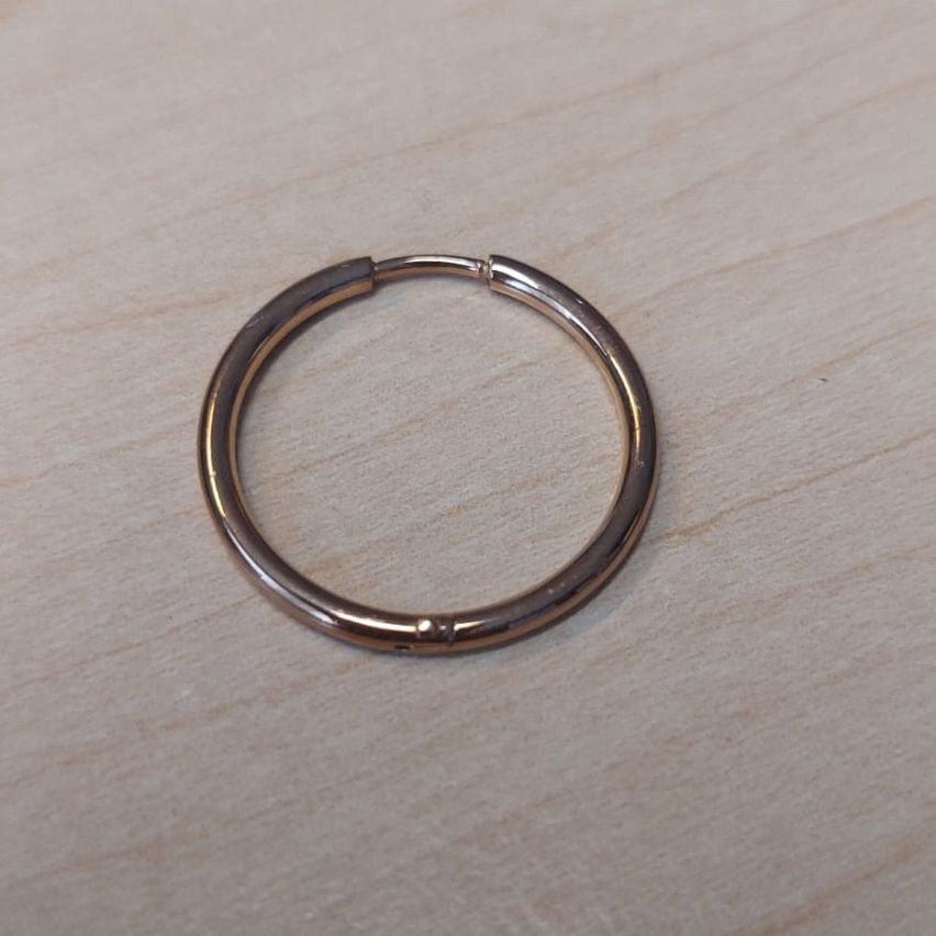 Ein Nahaufnahme eines kleinen, glänzenden, roségoldenen Rings mit glatter Oberfläche, der auf einer Holzunterlage ruht.