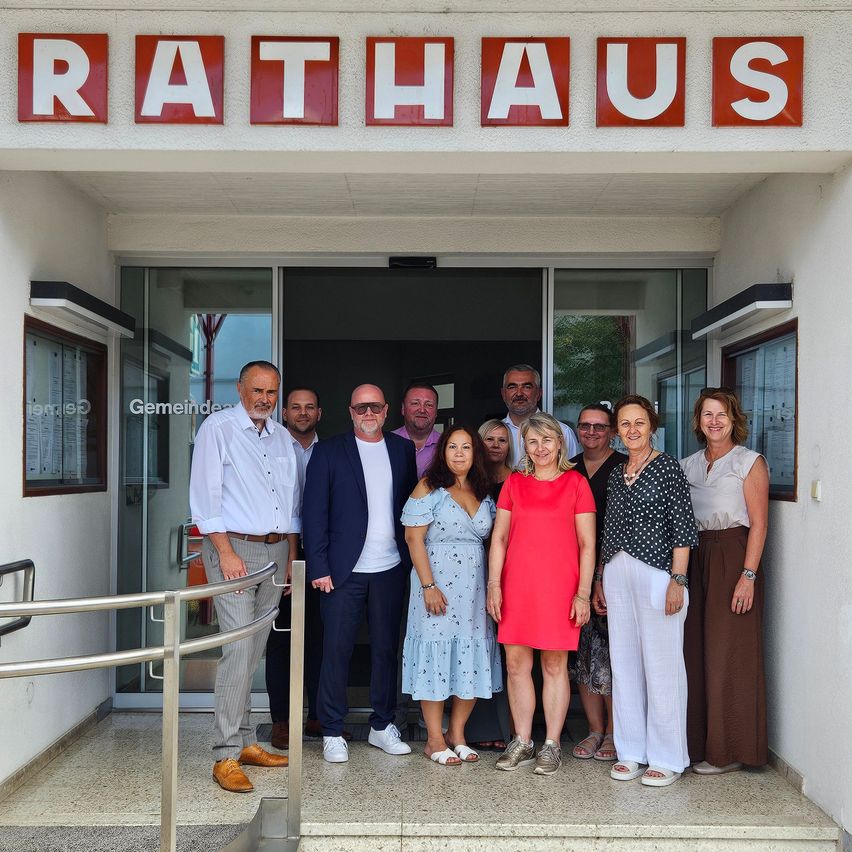 Eine Gruppe von Menschen steht vor einem Gebäude mit dem Wort Rathaus oben. Sie lächeln und posieren für ein Foto.