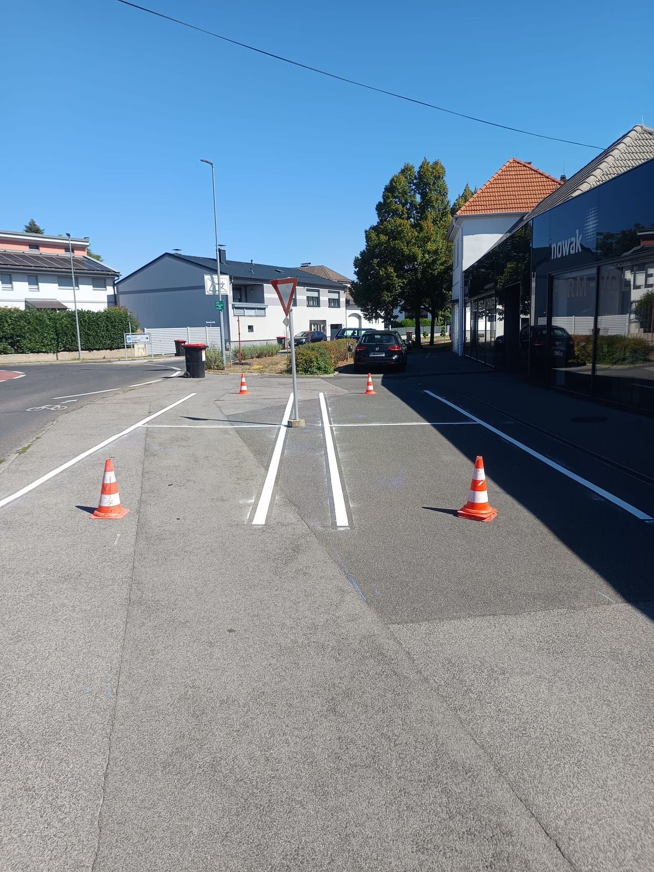 Ein leerer Parkplatz mit weißen Markierungen und Verkehrskegel. Ein Gebäude mit rotem Dach befindet sich rechts.