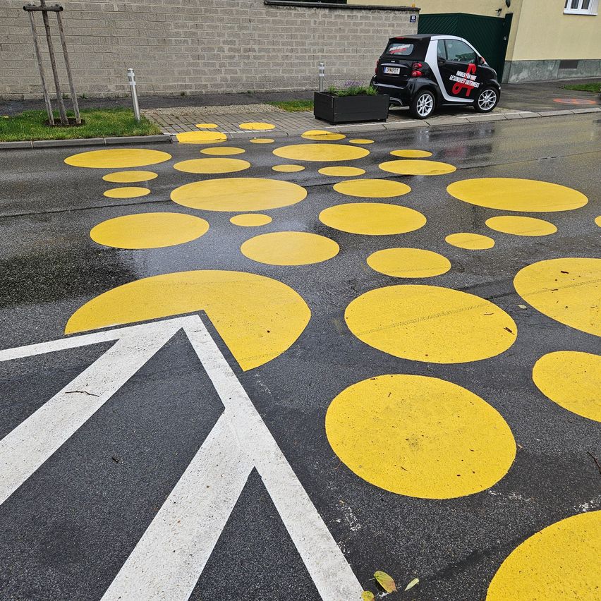 A parking lot with yellow circles and a white arrow pointing left. A black car is parked near a building.