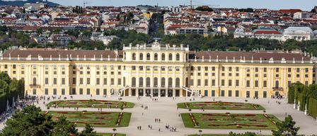 Ein Luftbild des Schönbrunner Schlosses mit seinen weitläufigen Gärten und der Stadtsilhouette im Hintergrund.