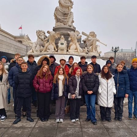 Eine Gruppe von Studenten posiert an einem bewölkten Tag vor einer großen Statue, alle in Winterkleidung und einigen Hüten.