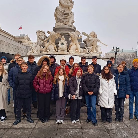Eine Gruppe von Studenten posiert an einem bewölkten Tag vor einer großen Statue, alle in Winterkleidung und einigen Hüten.