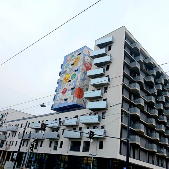 Ein Hochhaus mit einem großen Wandbild an seiner Seite verfügt über mehrere Balkone. Das Wandbild zeigt verschiedene farbige Schallplatten.
