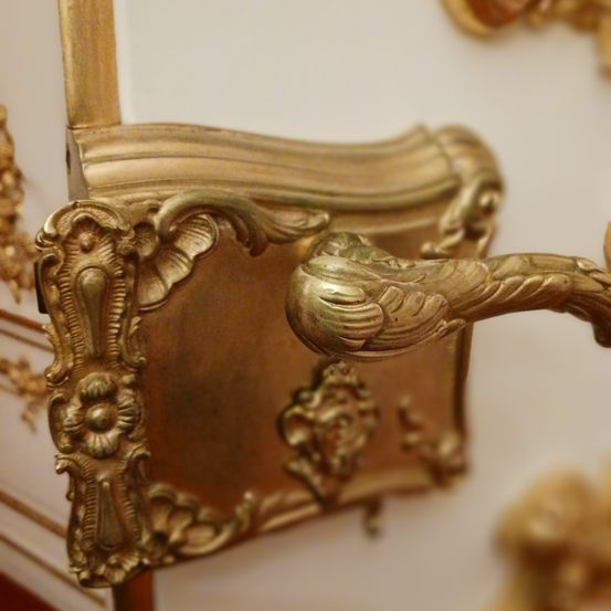 Eine Nahaufnahme eines goldfarbenen antiken Türgriffs mit aufwendigen Blumendesigns vor weißem Hintergrund.