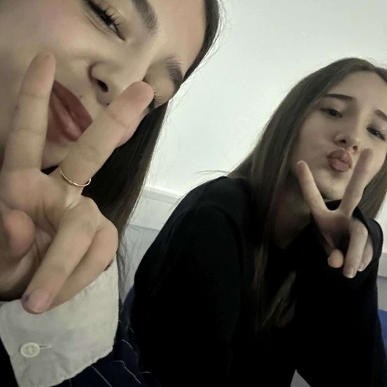 Zwei junge Frauen machen Friedenszeichen mit ihren Händen. Die Frau auf der linken Seite hat einen Ring am Finger. Die Frau auf der rechten Seite trägt ein schwarzes Oberteil.