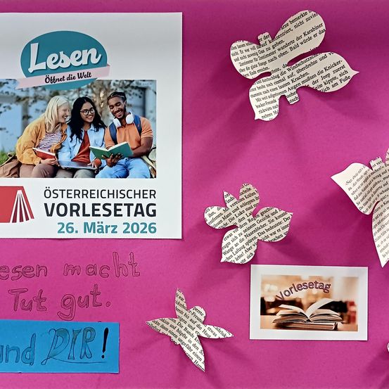 Poster für den österreichischen Vorlesetag am 26. März 2026 zeigt drei lächelnde Personen, die Bücher lesen. Dekorative Papierschmetterlinge sind um das Poster herum verstreut und verleihen ihm einen verspielten Touch.