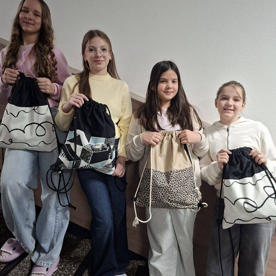 Vier junge Mädchen stehen zusammen und halten jeweils einen Rucksack mit einzigartigen Designs, was ihre Kreativität in einem schulischen Umfeld zeigt.