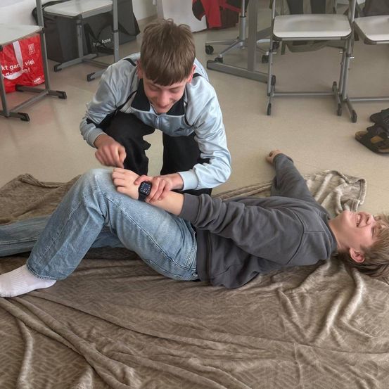 Zwei Jungen spielen auf einer Decke. Einer liegt auf dem Rücken, der andere kniet neben ihm und hält sein Handgelenk.