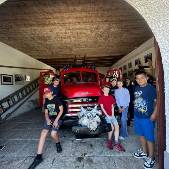 Gruppe von Kindern posiert vor einem roten Feuerwehrauto in einer Garage. Einige sind im Inneren des Fahrzeugs.