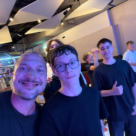 Eine Gruppe von Menschen steht zusammen in einem Raum, lächelt und posiert für ein Foto. Der Mann in der Mitte trägt eine Brille.