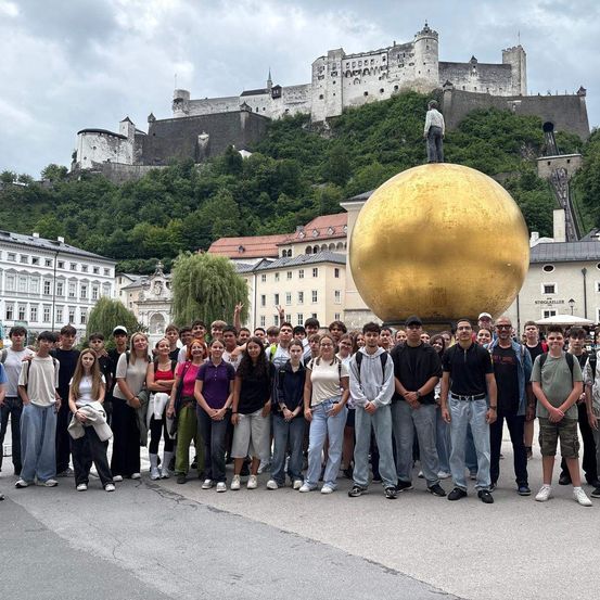 Eine Gruppe von Menschen steht vor einer goldenen Kugelskulptur mit einer Burg im Hintergrund.