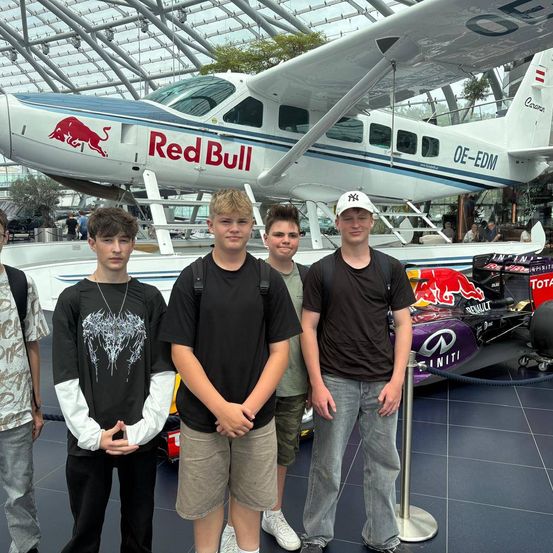 Fünf junge Männer stehen vor einem Red Bull Flugzeug und einem Formel 1 Auto in einem Museum.