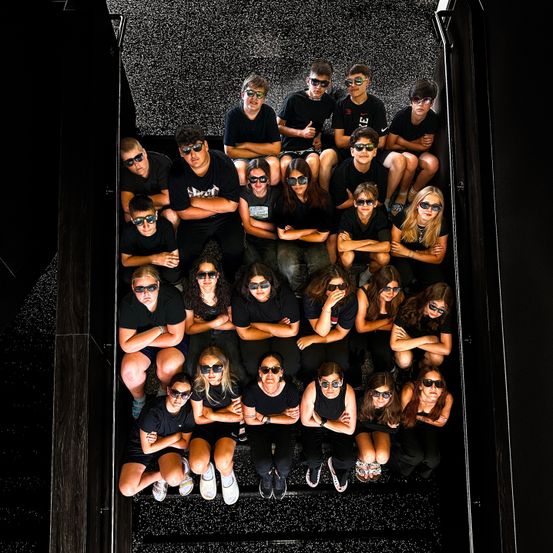 Eine Gruppe von Menschen in Sonnenbrillen und schwarzen T-Shirts posiert für ein Foto im Studio.