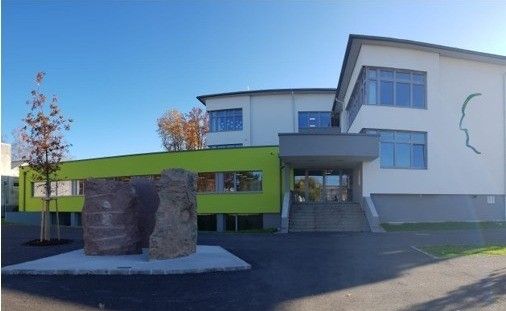 Ein modernes Gebäude mit grünen Akzenten und großen Steinen davor, unter einem klaren blauen Himmel.