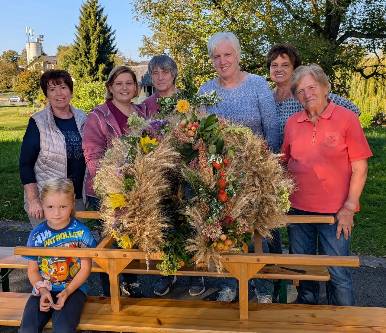 Eine Gruppe von Frauen und einem kleinen Mädchen stehen hinter einer Holzbank mit einer großen Blumendekoration in der Mitte.
