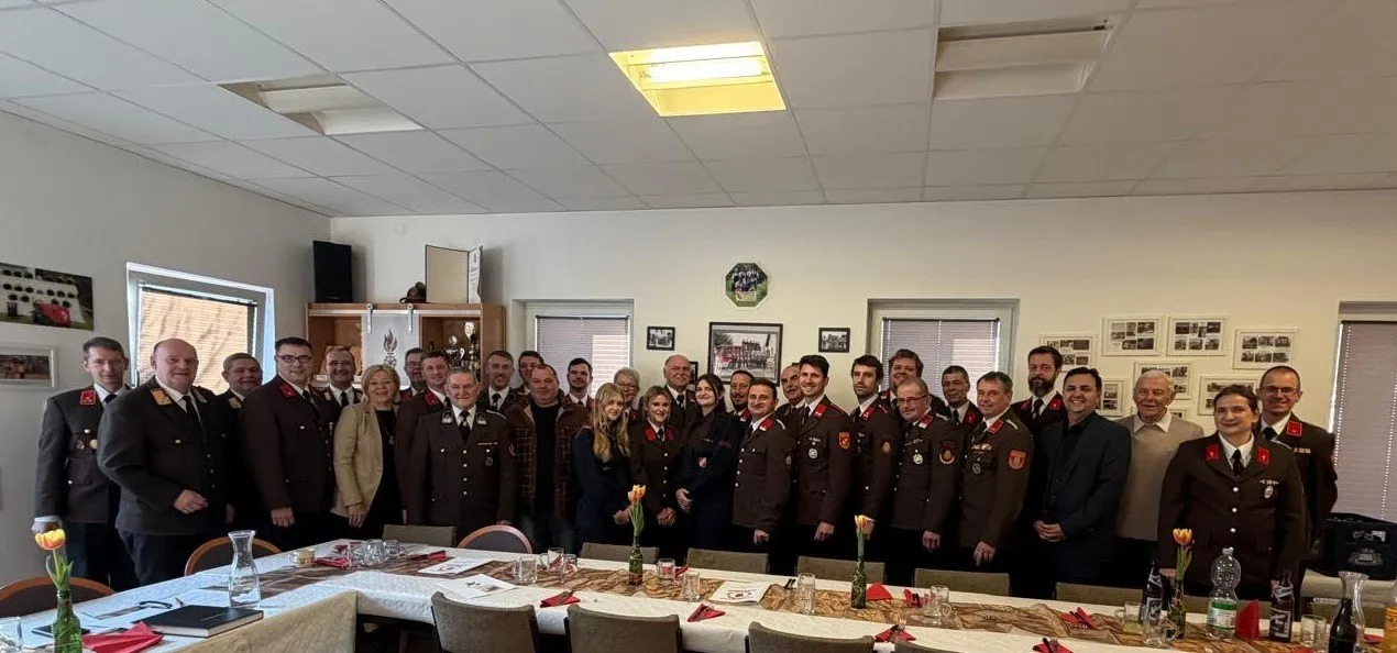 Eine Gruppe von Menschen in Uniform steht in einem Raum zusammen, mit einem langen Tisch davor, Gläsern und einer Blumenvase.