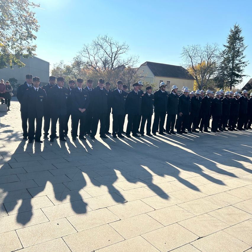 Eine Gruppe uniformierter Personen steht in einer Reihe auf einem gepflasterten Bereich. Sie tragen alle Hüte und Schuhe. Im Hintergrund befinden sich Bäume und Gebäude.