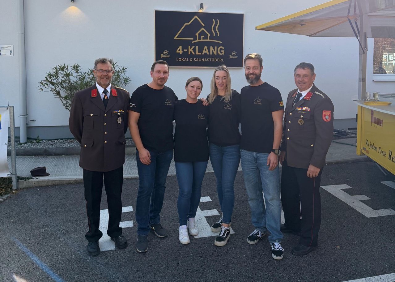 Fünf Personen, darunter zwei Frauen, stehen vor einem Gebäude namens 4-Klang. Sie tragen alle Uniformen und scheinen für ein Foto zu posieren.