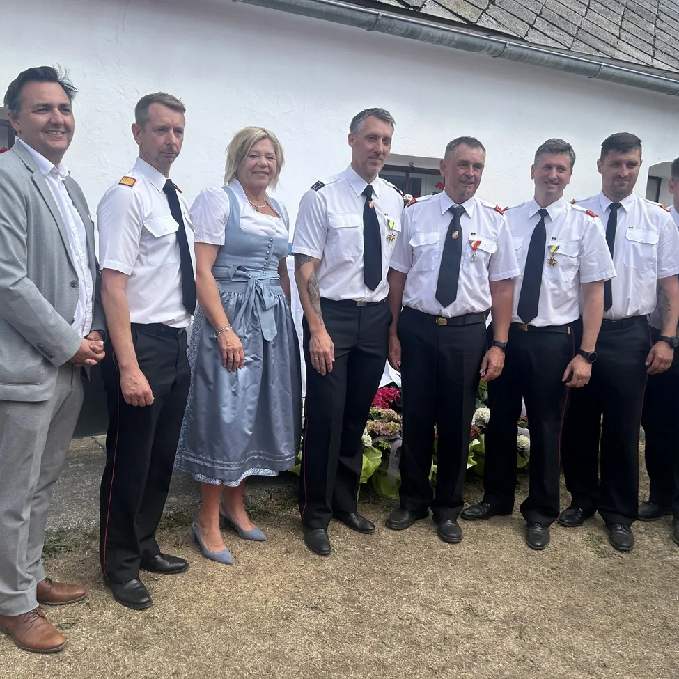 Eine Gruppe von Menschen in formeller Kleidung steht vor einem Gebäude, mit einer Frau in einem blauen Kleid unter ihnen.