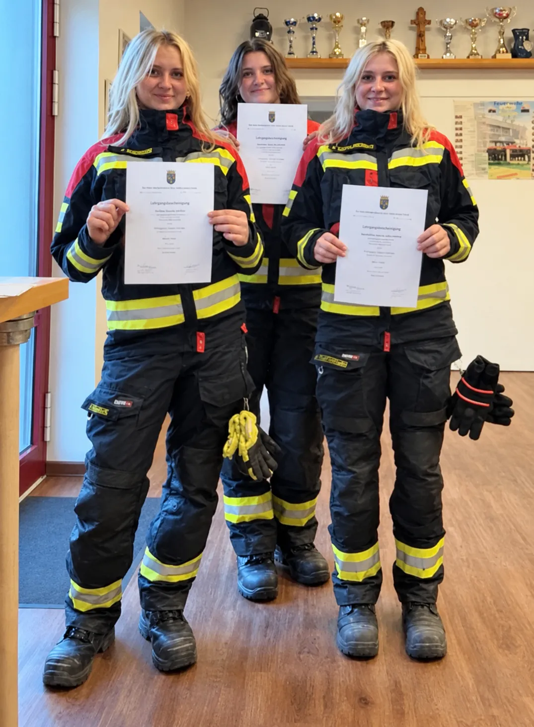 Drei Frauen in Feuerwehruniformen stehen zusammen und halten Urkunden in den Händen. Sie lächeln und posieren für ein Foto.