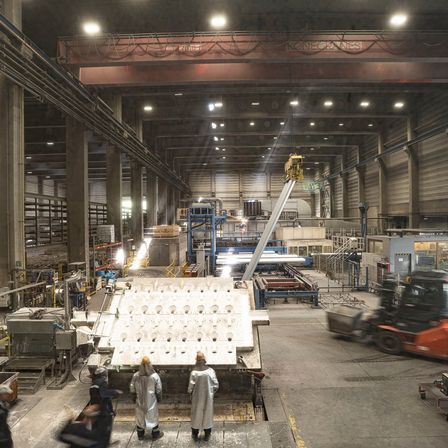 Ein Industriegebäude mit Arbeitern in Schutzanzügen in der Nähe einer großen Maschine, einem Gabelstapler und diversen Geräten und Maschinen.