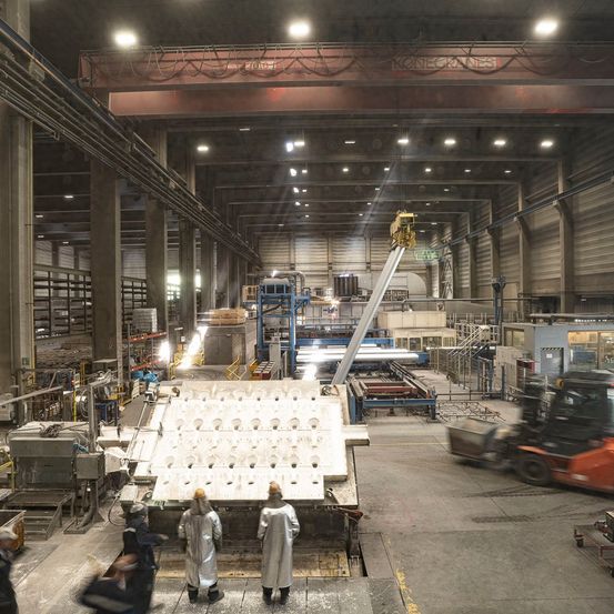 Ein Industriegebäude mit Arbeitern in Schutzanzügen in der Nähe einer großen Maschine, einem Gabelstapler und diversen Geräten und Maschinen.