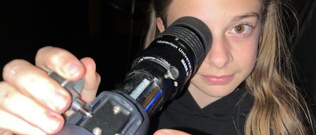 Ein junges Mädchen hält ein schwarzes Teleskop mit Hyperion Universal darauf und schaut hindurch.