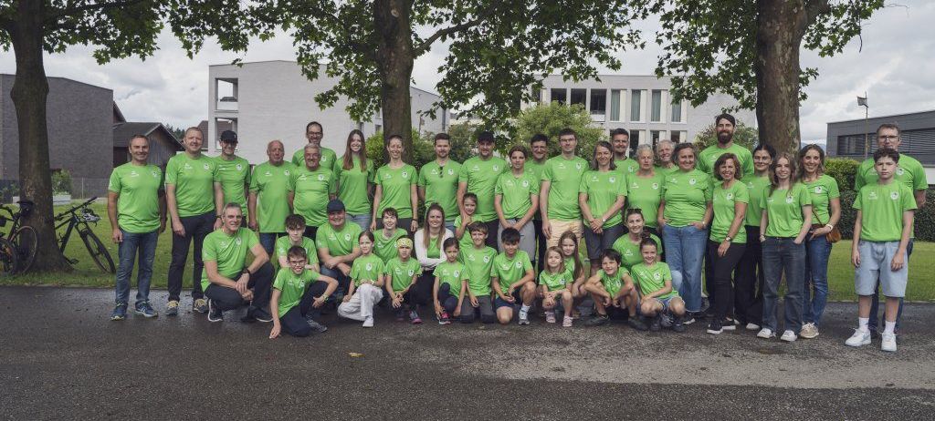 Eine Gruppe von Erwachsenen und Kindern in grünen Shirts posiert für ein Foto vor einem Gebäude.