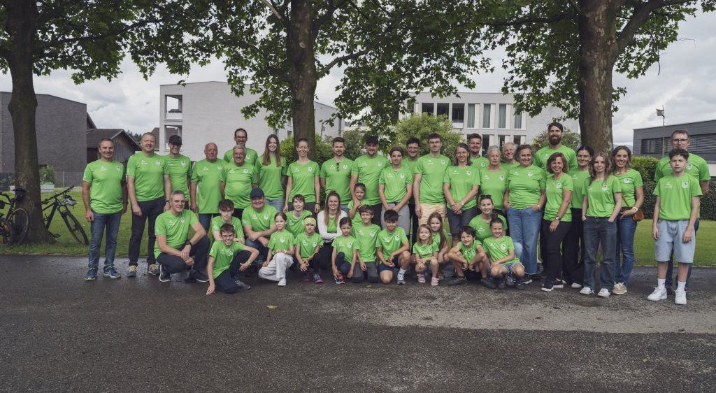 Eine Gruppe von Erwachsenen und Kindern in grünen Shirts posiert für ein Foto vor einem Gebäude.
